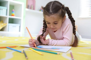Evde yerde kalemle çizen sevimli küçük kız.