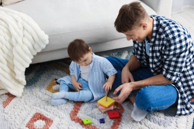 Gülümseyen erkek dadı ve sevimli küçük çocuk evde oyuncaklarla oynuyorlar.