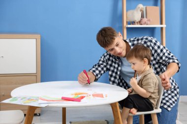 Erkek dadı ve küçük şirin çocuk beyaz masaya resim çiziyorlar.