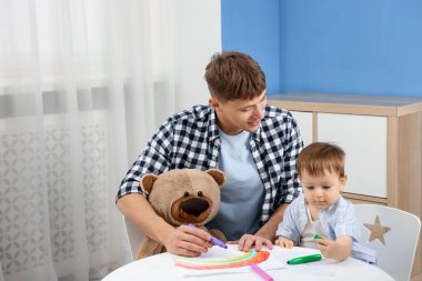 Gülümseyen erkek dadı ve beyaz masaya resim çizen sevimli küçük çocuk. Metin için boşluk