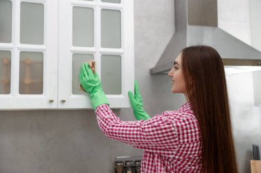 Mutfaktaki dolaptaki tozları silen kadın.