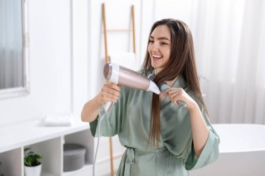 Bornozlu gülümseyen kadın saçını saç kurutma makinesiyle şekillendiriyor ve banyoda fırçalıyor. Metin için boşluk