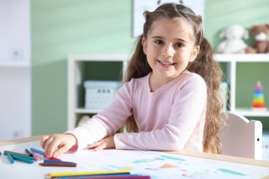 Masada pastel boyayla resim çizen sevimli küçük kız.