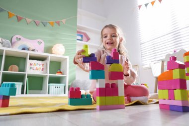 Oyun odasında yerde oyuncakla oynayan mutlu küçük kız, düşük açı.