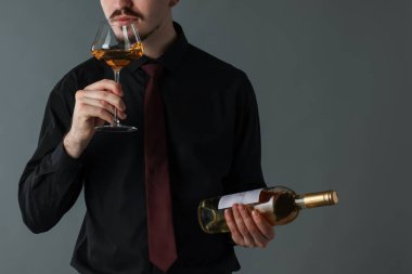 Profesyonel şarap garsonu gri arka planda beyaz şarap tadıyor.