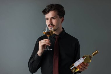 Profesyonel şarap garsonu gri arka planda beyaz şarap tadıyor.