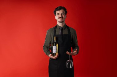 Kırmızı arka planda beyaz şarap ve cam şişesi olan profesyonel şarap garsonu.