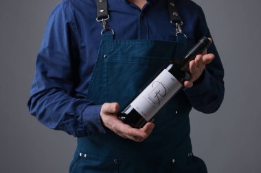 Gri arka planda kırmızı şarap şişesi olan profesyonel şarap garsonu.