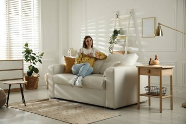 Evdeki kanepede dinlenen mutlu bir kadın.