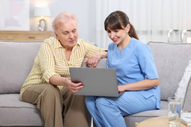 Huzurevinde yaşlı bir kadına dizüstü bilgisayar kullanmayı öğreten bakım işçisi.