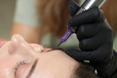 Güzellik uzmanı genç bayana kalıcı kaş makyajı yapıyor.