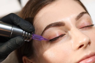 Güzellik uzmanı genç bir kadına kalıcı göz kalemi makyajı yapıyor.