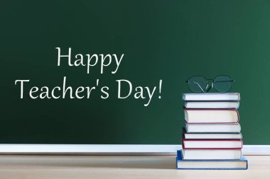 Öğretmenler Günün kutlu olsun! Yeşil karatahtanın yanında gözlüklü istiflenmiş kitaplar.