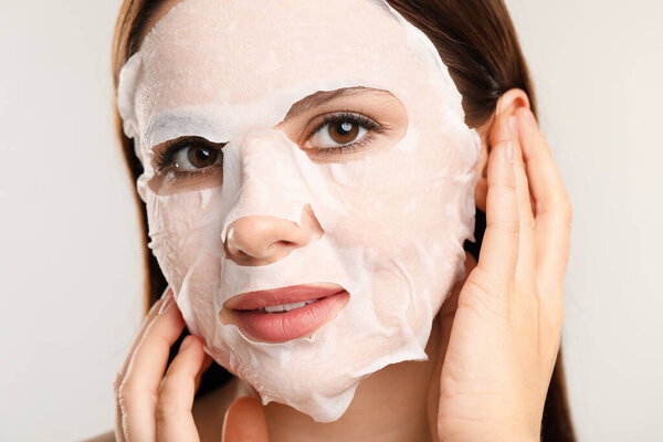 Woman with facial mask on light grey background, closeup