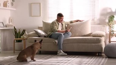 Akıllı telefonlu genç adam evdeki şirin köpeğin yanındaki kanepede dinleniyor.