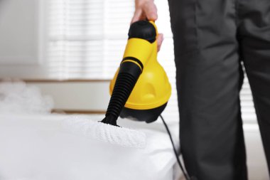 Haşere kontrol işçisi yatağı temizliyor, kapalı alanda buhar temizleyicisiyle, yakın plan