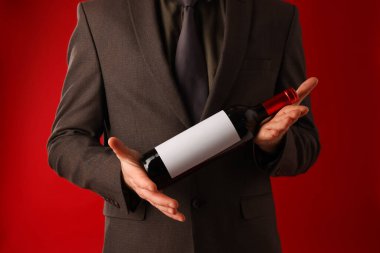 Kırmızı arka planda şarap şişesi olan profesyonel şarap garsonu, yakın plan.