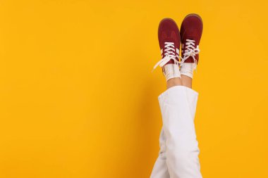 Sarı arka planda şık bordo ayakkabılar giyen bir kadın, yakın plan. Metin için boşluk