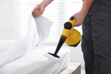 Haşere kontrol işçisi yatağı temizliyor, kapalı alanda buhar temizleyicisiyle, yakın plan