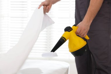 Haşere kontrol işçisi yatağı temizliyor, kapalı alanda buhar temizleyicisiyle, yakın plan