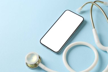 Sağlığınıza. Açık mavi arka planda akıllı telefon ve steteskop, yakın plan. Metin için boşluk