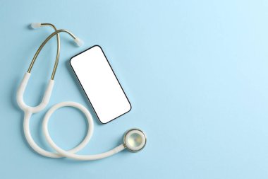 Sağlığınıza. Açık mavi arka planda akıllı telefon ve steteskop, düz konum. Metin için boşluk