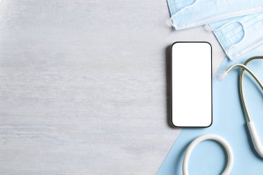 Sağlığınıza. Akıllı telefon, steteskop ve ışık desenli masada duran tıbbi maskeler, düz yatak. Metin için boşluk