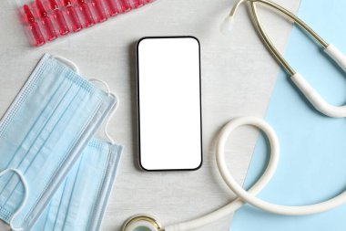 Sağlığınıza. Akıllı telefon, steteskop, sıvı ve tıbbi maskeli ampuller açık dokulu masa, düz yatak