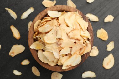 Kurutulmuş sarımsak taneleri ve kase koyu dokulu masa, düz uzanmış.