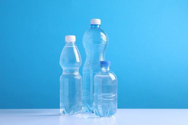 Açık mavi arka planda beyaz masada farklı boyutlarda su şişeleri