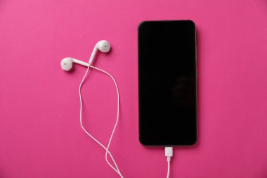 Pembe arka planda kulaklıklı akıllı telefon, üst görüş.