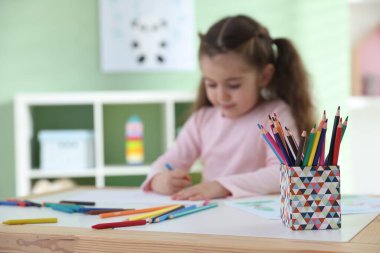 Masada pastel boyayla resim çizen şirin bir kız. Seçici bir odak noktası var. Metin için boşluk