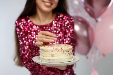 Doğum günü kutlaması. Kekin içine mum koyan kadın açık gri arka planda, yakın plan