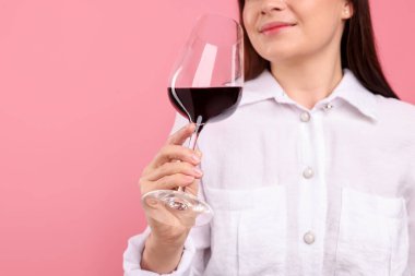 Profesyonel şarap garsonu pembe arka planda kırmızı şarap tadıyor.