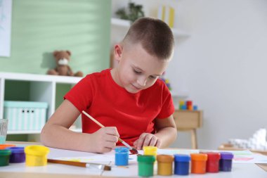 Masada fırçayla resim yapan şirin bir çocuk.