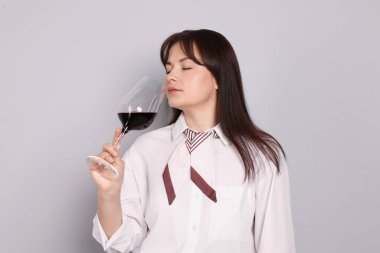 Profesyonel şarap garsonu açık gri arka planda kırmızı şarap tadıyor.