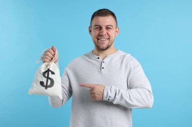 Açık mavi arka planda para dolu çantayı gösteren mutlu adam.