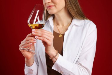 Profesyonel şarap garsonu kırmızı arka planda şarap tadıyor, yakın plan.