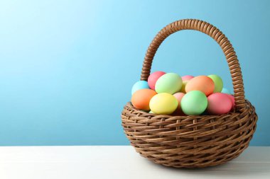 Güzel dekore edilmiş Paskalya yumurtaları hasır sepetin içinde beyaz ahşap masa üzerinde açık mavi arkaplan, metin için boşluk