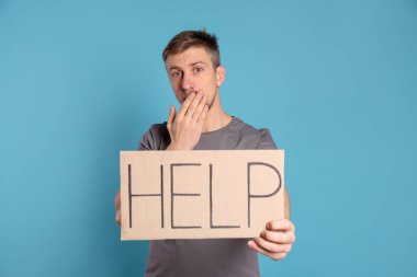 Mutsuz adam elinde kelime yazılı karton tabela açık mavi arka planda yardım