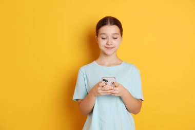 Turuncu arka planda akıllı telefonu olan genç bir kız, mesaj atmak için yer var.