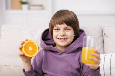 Evdeki kanepede bir bardak taze portakal suyu olan çocuk.