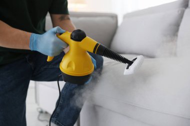 Haşere kontrol işçisi kanepeyi temizliyor. Kapalı alanda buhar temizleyicisi var.