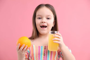 Bardakta portakal suyu ve pembe arka planda taze meyve olan küçük kız.