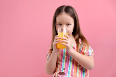 Pembe arka planda bir bardak portakal suyu olan küçük kız, mesaj için yer var.