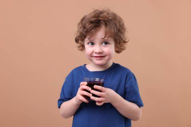 Kahverengi arka planda bir bardak nar suyu olan küçük bir çocuk.
