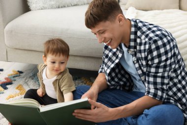 Gülümseyen erkek dadı evde yerde yatan şirin çocuğa kitap okuyor.