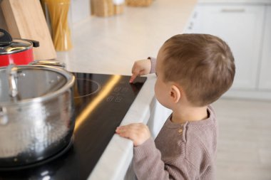 Evde çocuk güvenliği. Küçük çocuk mutfakta ocakla oynuyor.
