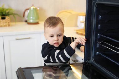 Evde çocuk güvenliği. Küçük çocuk mutfakta fırın açıyor.