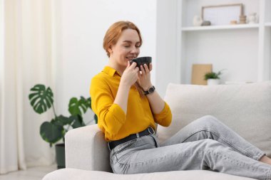 Evdeki kanepede bir fincan aromatik kahveyle güzel bir kadın.